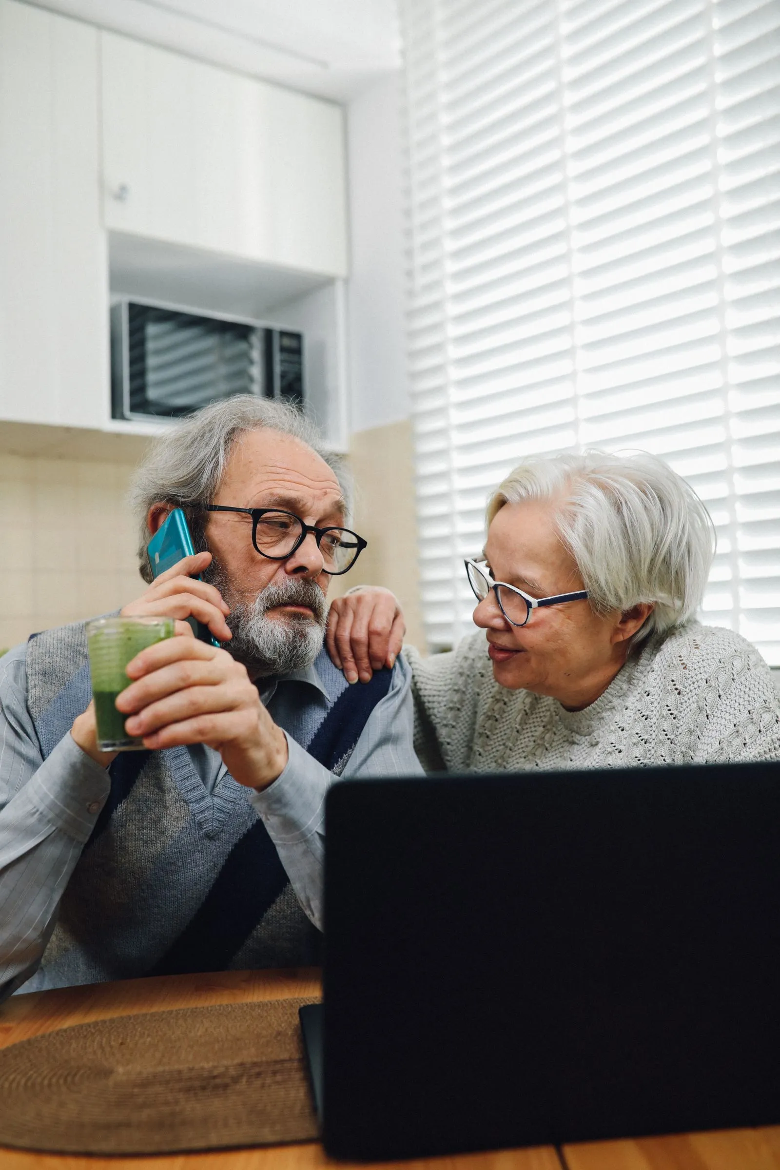 An older couple in their kitchen, one of them on a phone call