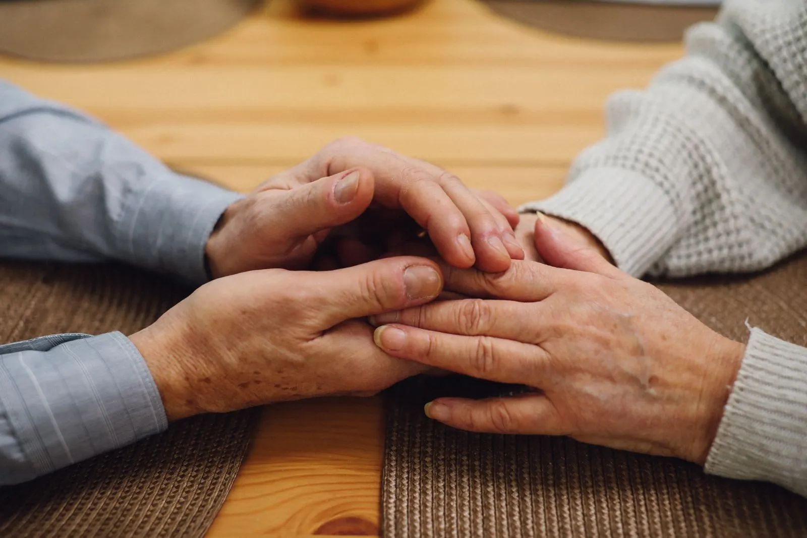 An older couple's hands held together on a wooden table