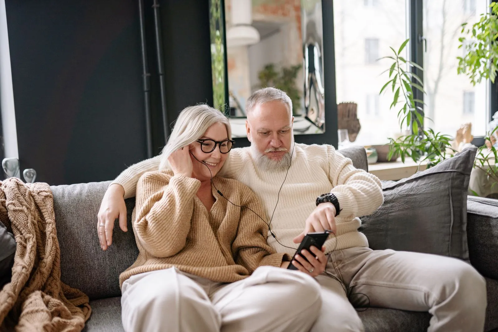 An older couple relaxing together on their couch at home, sharing a phone